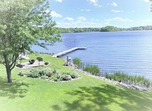 A lakeside property with a dock extending into the water, surrounded by well-maintained grass and a variety of plants. - Charming 2-bedroom house with WiFi, AC on Knife Lake in Mora Minnesota. (Mora)