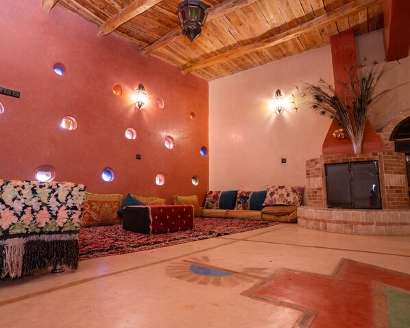 A cozy living room with a red wall, circular windows, and a brick fireplace. - Dar Badiawarda (Ait Taguella)
