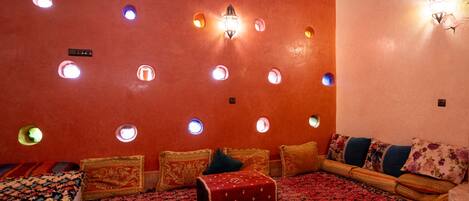 A room with a red carpet, a sofa with patterned cushions, a red ottoman, and a wall with circular light fixtures.