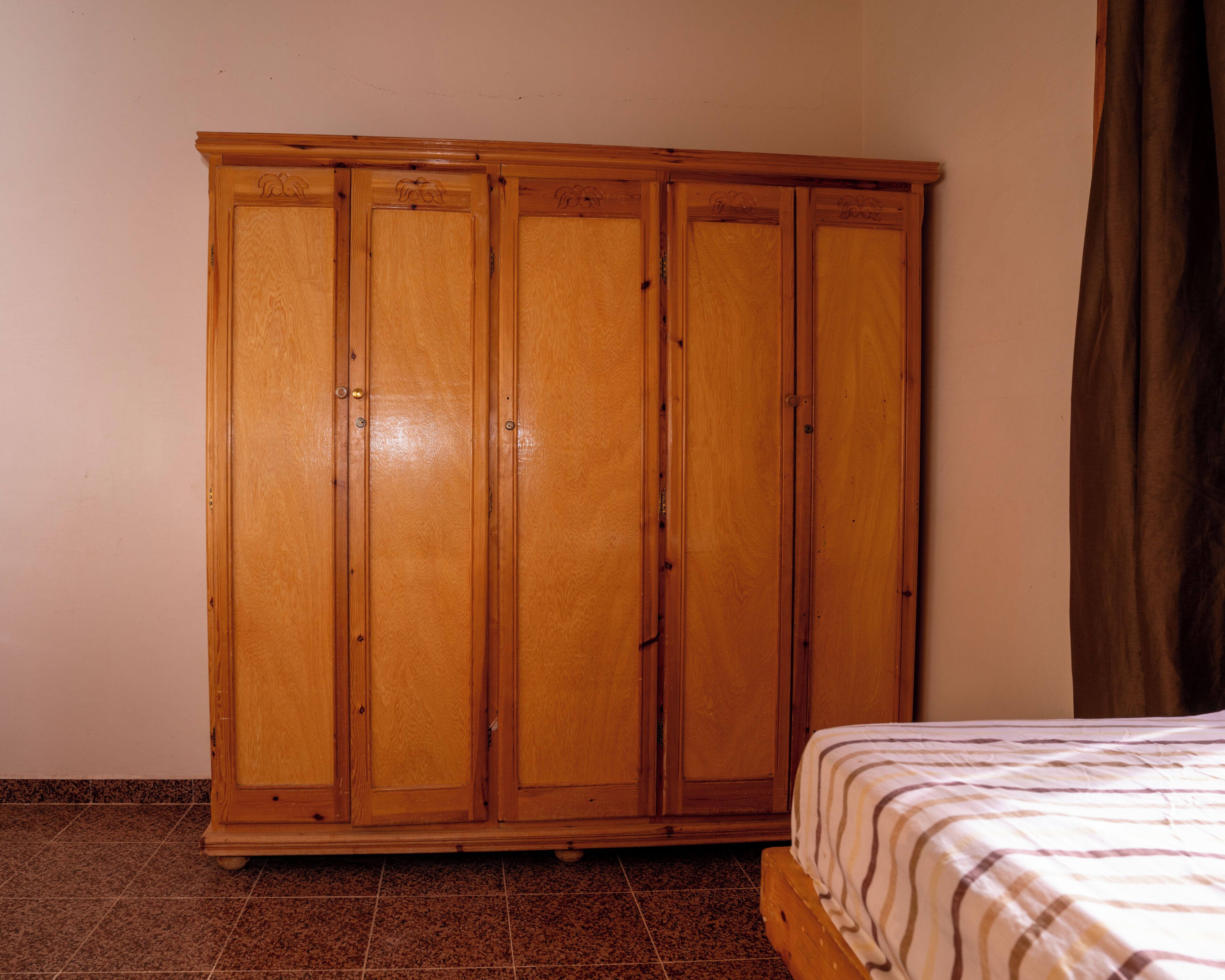 Un dormitorio con un armario de madera, una cama con cubrecama a rayas y una cortina marrón.
