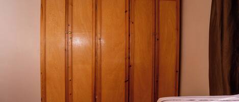 Un dormitorio con un armario de madera, una cama con cubrecama a rayas y una cortina marrón.