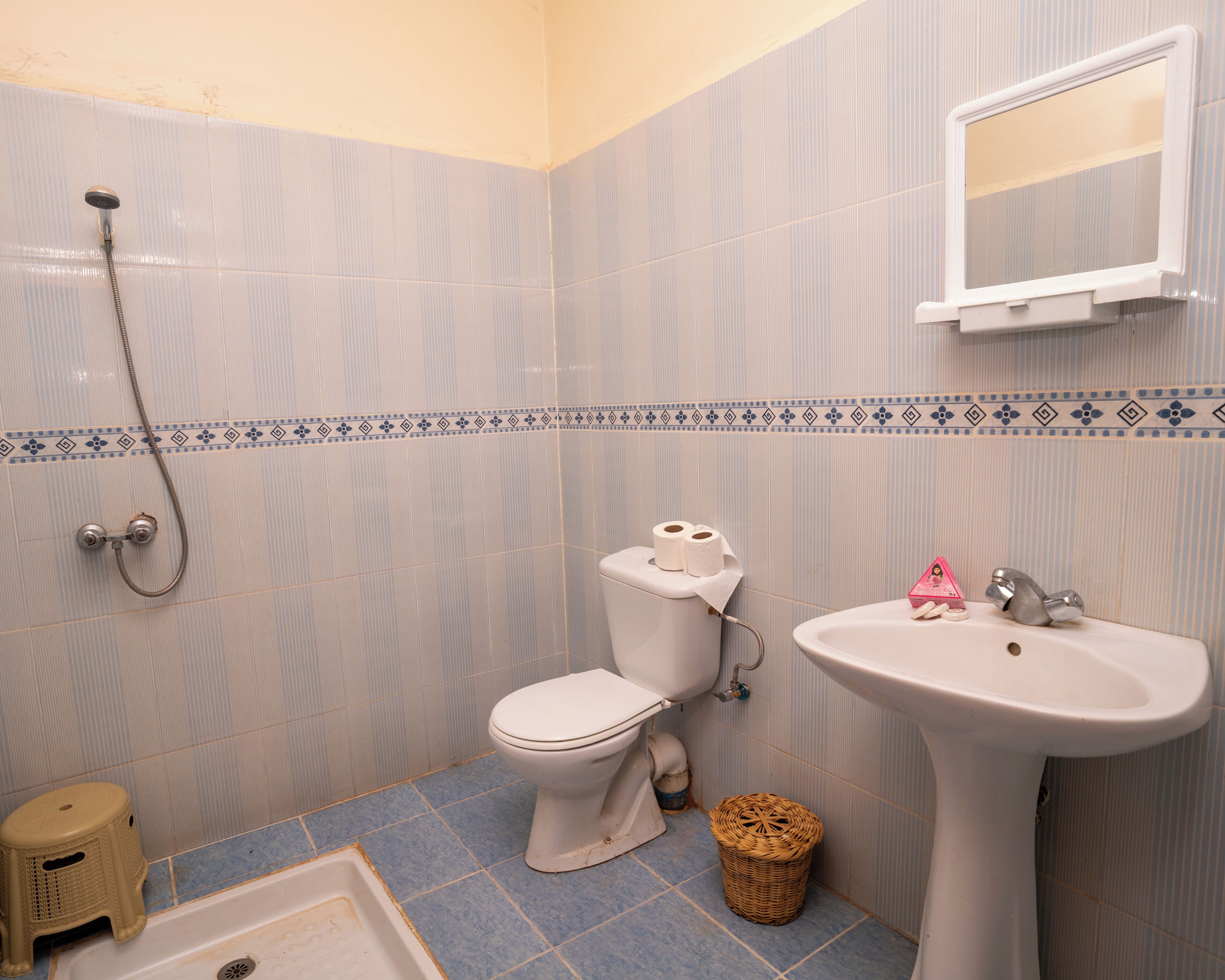 A bathroom with a toilet, sink, shower, and a small stool.