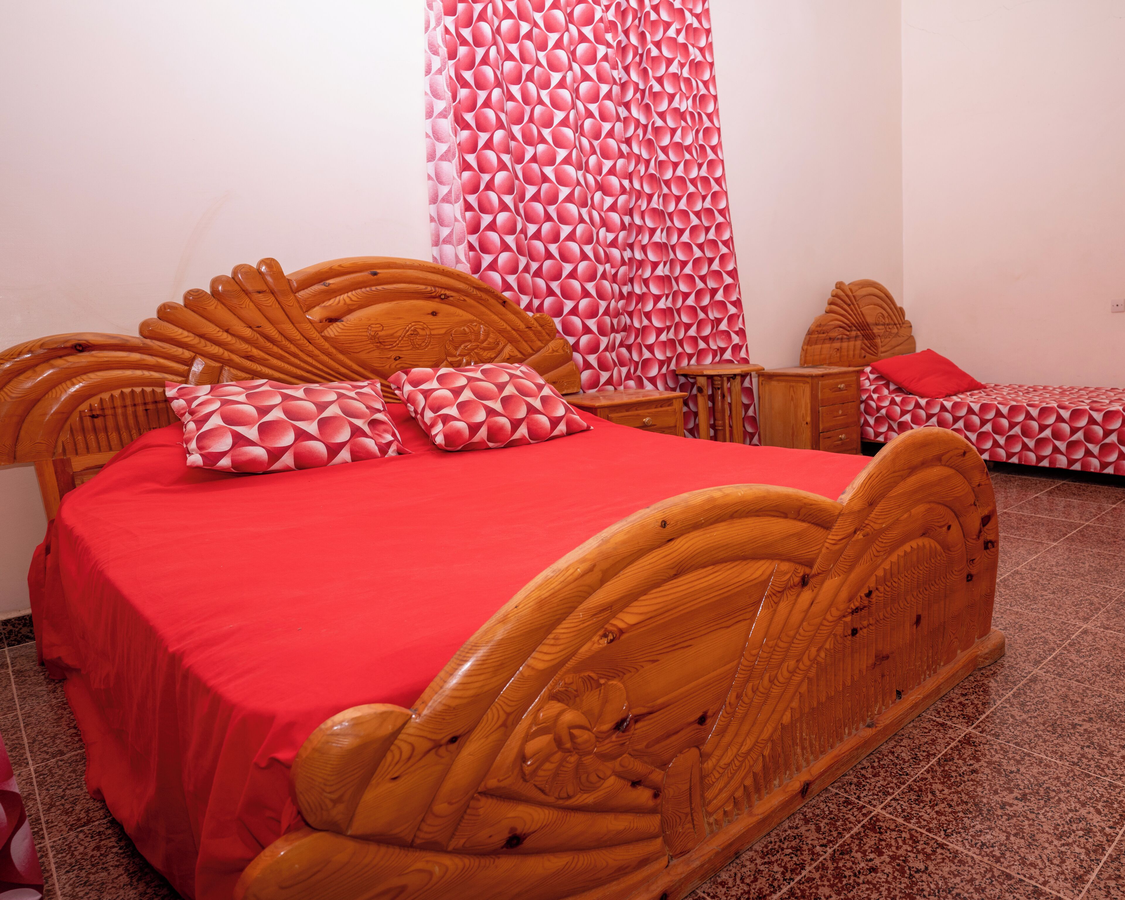 A room with a wooden bed, a small bedside table, and a red bedspread.
