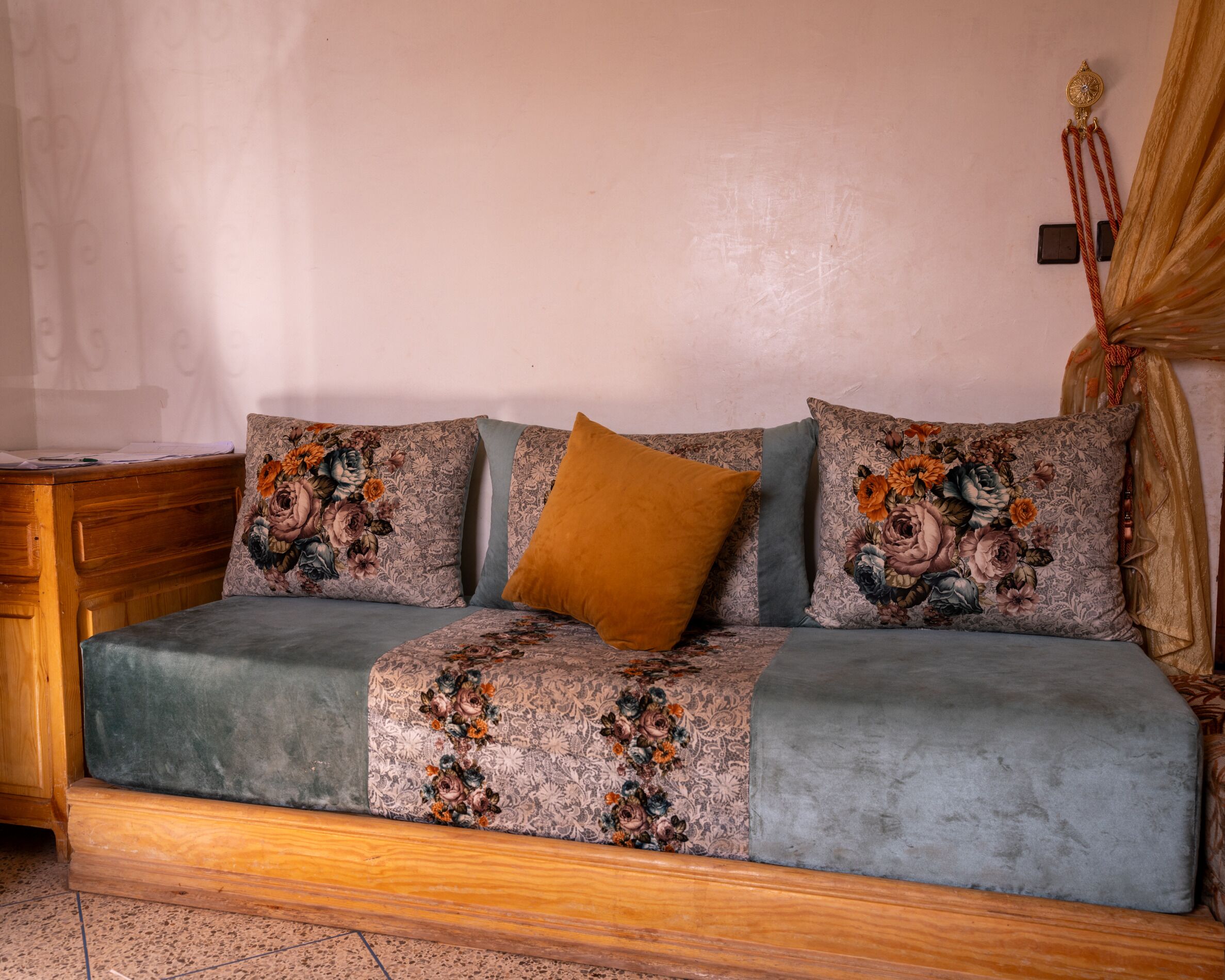 Un canapé recouvert d’un tissu à motifs floraux, un coussin de couleur moutarde et une petite table d’appoint en bois.