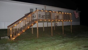 A wooden deck with railings and string lights, an American flag, and a white building in the background.