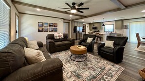 A spacious living room with a large sofa, a smaller sofa, and a coffee table. There is a ceiling fan and recessed lighting.