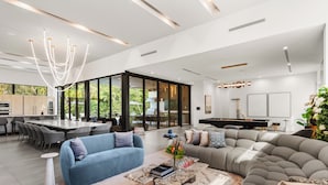 A modern living room with a blue sofa, a grey sectional, and a dining area with a large table. - Villa Maya: A Luxury Retreat in North Miami Beach (North Miami Beach)