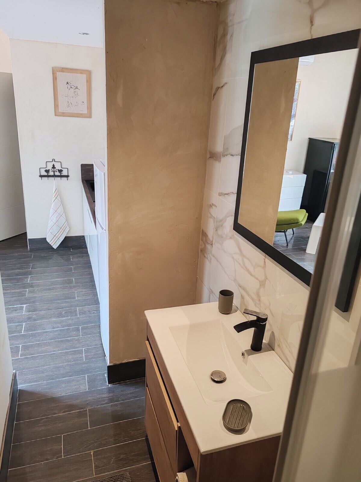 Un baño moderno con pared de mármol, un espejo grande, un lavabo blanco y un perchero para toallas.