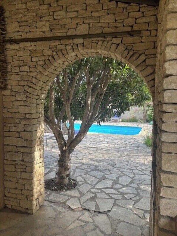 Stunning stone archway frames a serene pool area with a clear blue pool surrounded by a stone-tiled deck.