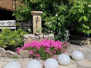 Stroll through the serene garden, surrounded by vibrant flowers and a soothing stone fountain featuring a carved figure.