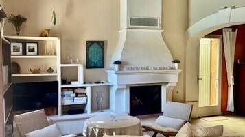 A living room with a fireplace, white sofas, a coffee table, and wooden beams on the ceiling.