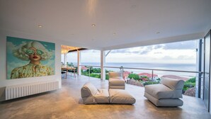A spacious balcony with a view of the sea, a modern sofa, and a large painting on the wall. - Your own private beach resort: HIGH-END VILLA CASA CAS ABAO  (Cas Abao)