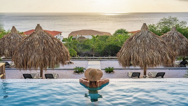 A poolside view with a person relaxing, overlooking a beach and ocean. - Your own private beach resort: HIGH-END VILLA CASA CAS ABAO  (Cas Abao)