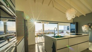 A modern kitchen with a large island, a view of the ocean, and a dining area with a table and chairs. - Your own private beach resort: HIGH-END VILLA CASA CAS ABAO  (Cas Abao)