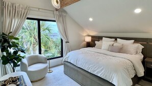 A modern bedroom with a large bed, a round chair, a small table, and a large window with curtains.