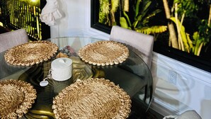 A round glass table with woven placemats, a white candle, and a vase.