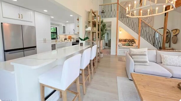 A spacious kitchen with a central island, white bar stools, and a staircase leading to an upper level.