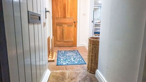 A hallway with a wooden door, a blue rug, and a welcome mat at the entrance. - River Dance Cottage (Leyburn)