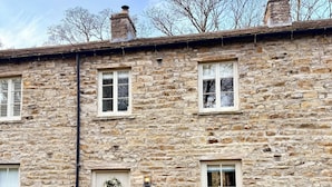 A stone building with a door, windows, and a small outdoor seating area with chairs and a table. - River Dance Cottage (Leyburn)