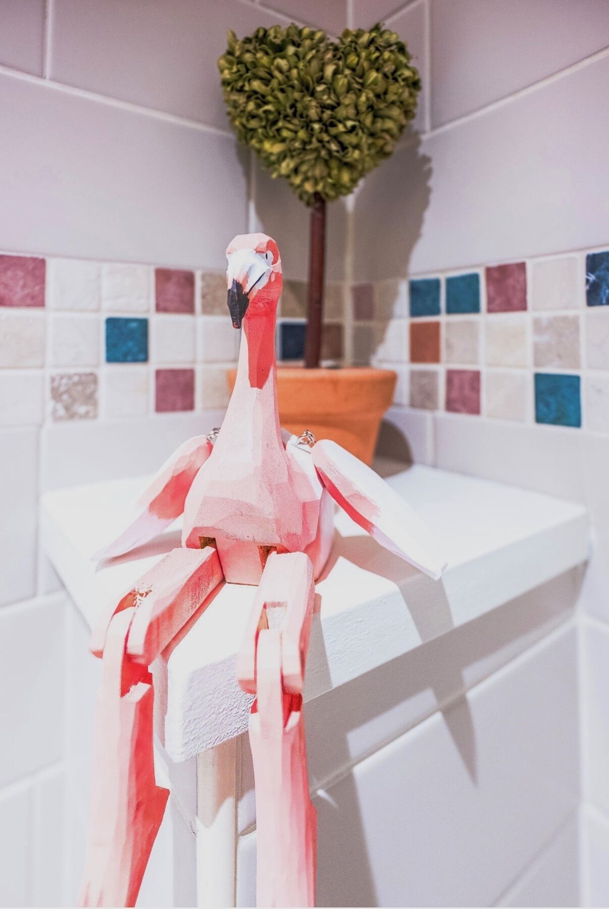 A bathroom with a white bathtub, a heart-shaped plant, and a tiled wall with multicolored tiles.