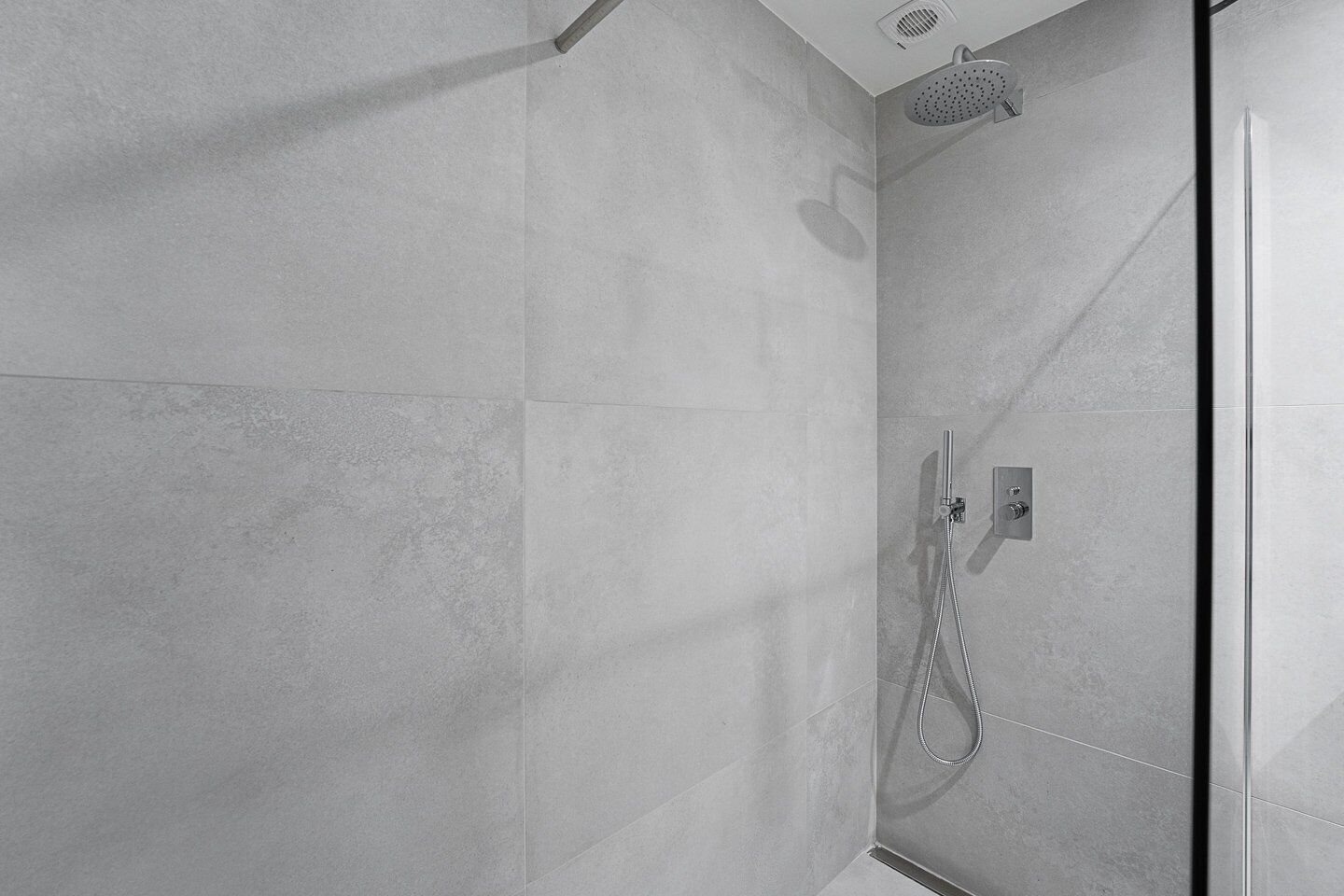 Ducha moderna con cabezal de ducha de mano y panel de control en la pared.