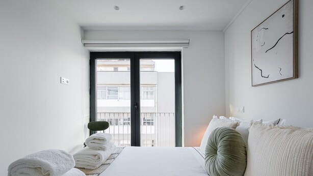Ein Hotelzimmer mit einem Bett, einem Sessel, einem Fenster mit Blick auf Gebäude und einem Bild an der Wand.