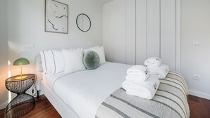 Ein modernes Schlafzimmer mit einem großen Bett, einem Nachttisch mit Lampe und einem runden, an der Wand befestigten Spiegel.