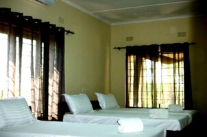 Quarto de hotel com duas camas de solteiro, uma janela com cortinas e uma parede simples.