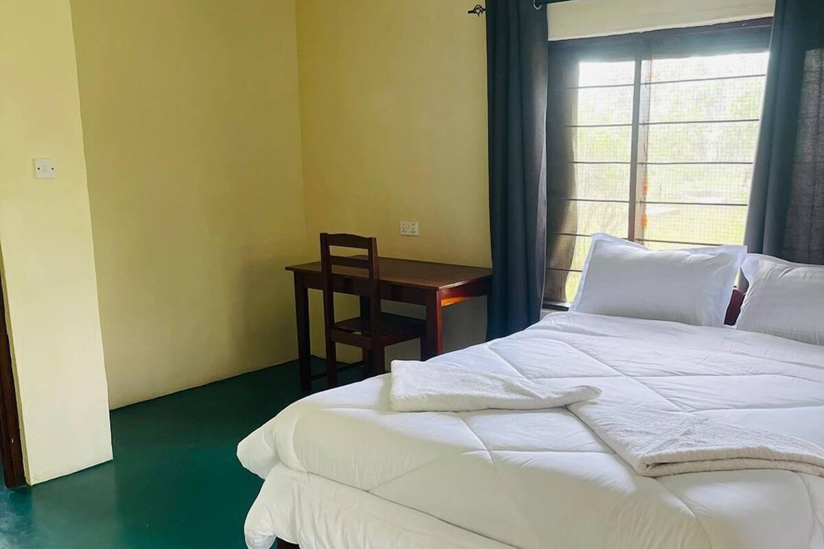 Une chambre à coucher avec un lit, une petite table, une chaise et une fenêtre avec des rideaux.
