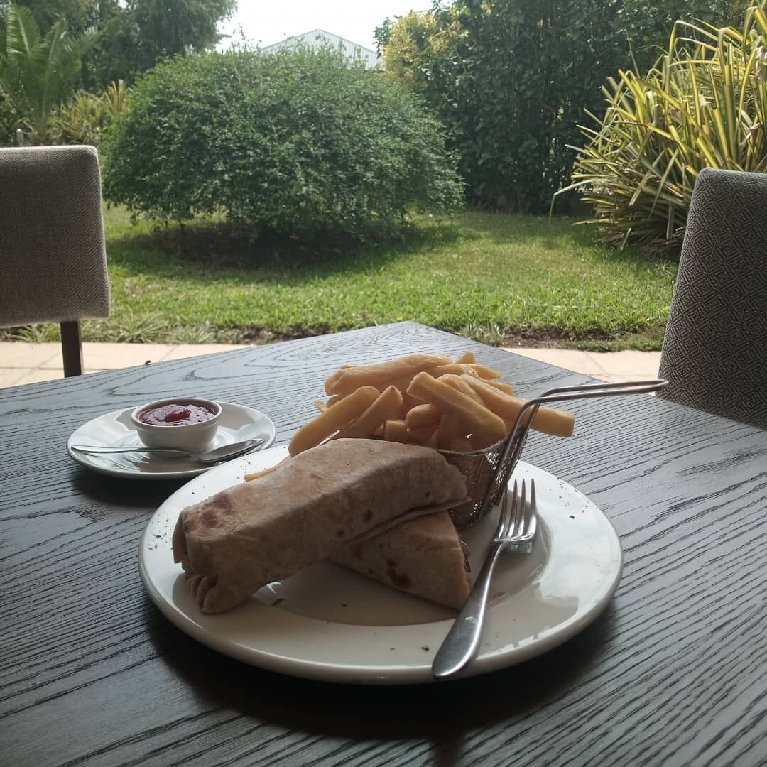 Ein Teller mit einem Sandwich, Pommes und einer kleinen Sauce auf einem Tisch im Freien.