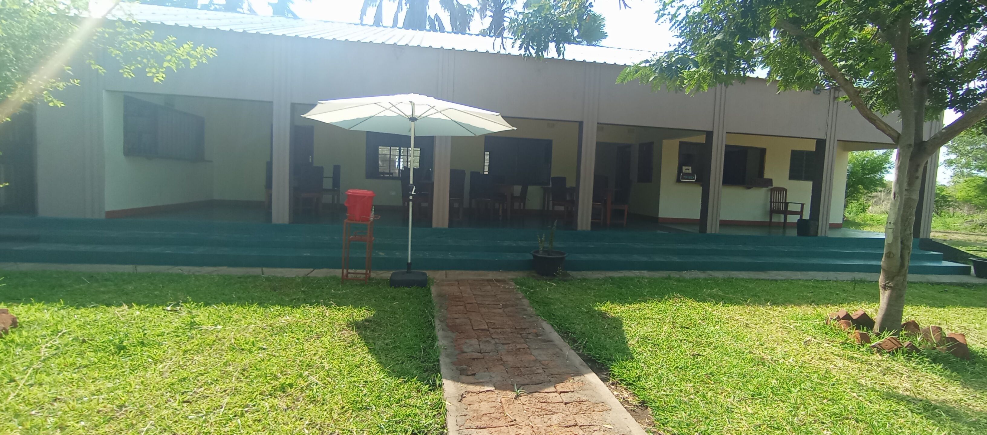 A building with a covered outdoor seating area, a pathway leading to the entrance, and a tree to the right.