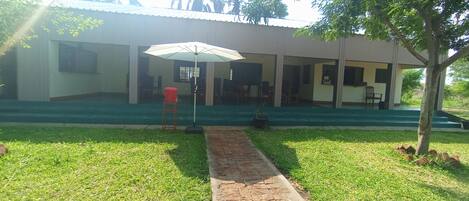 A building with a covered outdoor seating area, a pathway leading to the entrance, and a tree to the right.