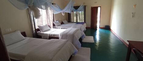 A hotel room with three beds, a green floor, and a window with curtains.