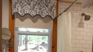 A bathroom with a white sink, a window with a view of trees, and a shower area. - Blueberry Hill Motel (Long Lake)