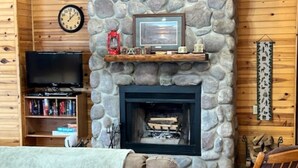 A cozy living room with a stone fireplace, wooden walls, a television, and a bookshelf.