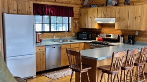 A cabin-style kitchen with wooden cabinets, a refrigerator, a stove, and bar stools.