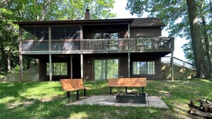 A two-story cabin with a balcony, a fire pit, and two benches in front.