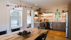 Une cuisine moderne avec une table à manger en bois, des appareils électroménagers en acier inoxydable et un luminaire suspendu.