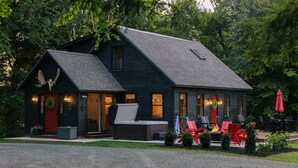 Un chalet à l’extérieur en bois sombre, doté d’une cheminée, d’un espace salon extérieur et d’une sculpture d’oiseau sur le toit.