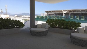 A rooftop terrace with wicker furniture and a view of a swimming pool and distant mountains. - Apartamento Náutico 300 (Nuevo Nayarit)