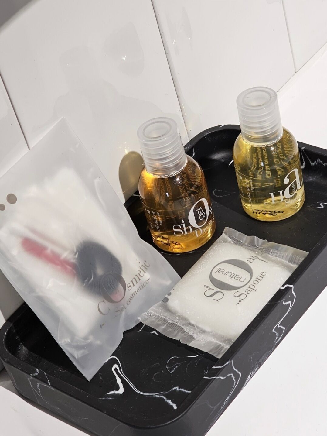 A black tray with two bottles of liquid soap and a plastic bag with a red object.