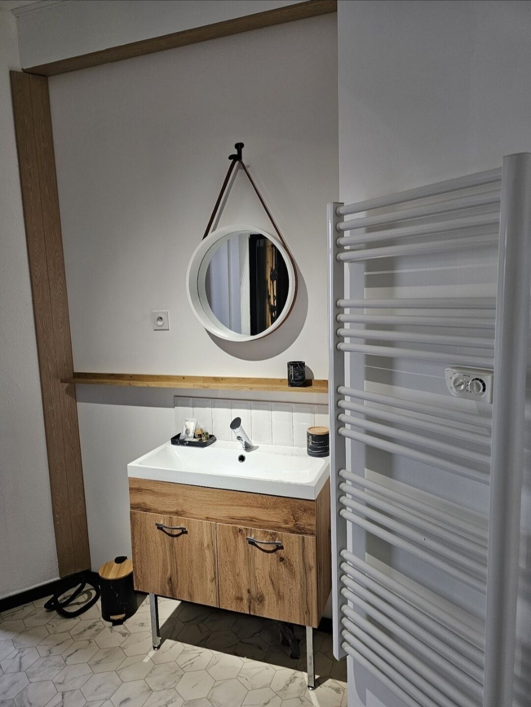 Une salle de bain avec un meuble-lavabo en bois, un miroir rond, un lavabo blanc et un porte-serviettes.