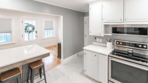 A kitchen with white cabinets, a stainless steel oven, and a bar area with stools. - White Mountain Escape (Littleton)
