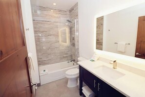 Bathroom features a glass-enclosed shower, white toilet, and modern vanity with a large mirror.