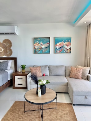A modern living room with a sofa, a coffee table, a side table with a plant, and two paintings on the wall. - Luxury Oceanfront Studio • Stunning Views • Pool • Balcony + Free Parking (Fajardo)