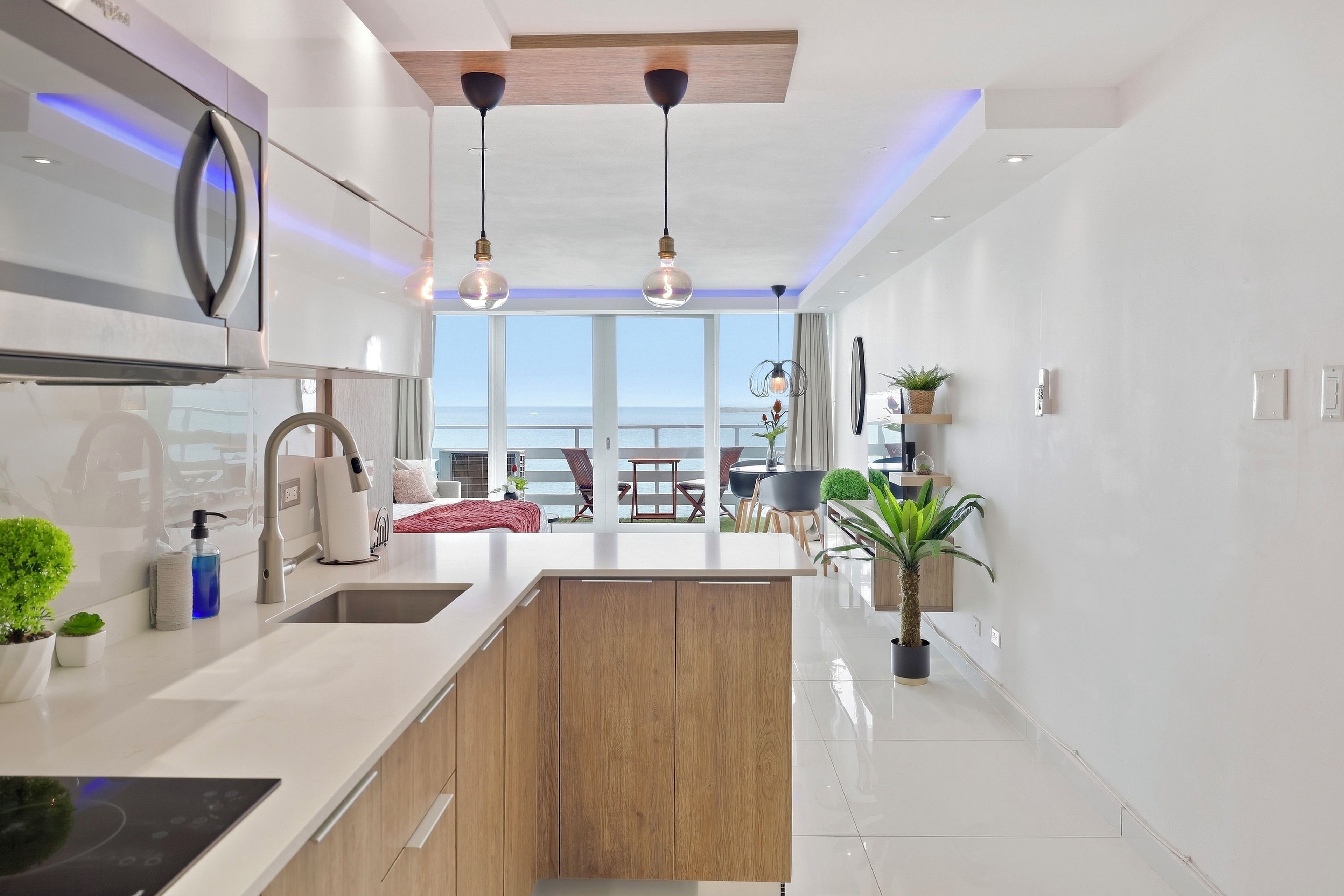 A modern kitchen with a central island, pendant lighting, and a view of the sea.