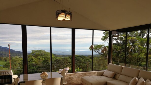 A modern living room with large windows, a dining area, and a sofa. - Cozy cabin surrounded by nature with breathtaking views for total relaxation (Heredia Province)