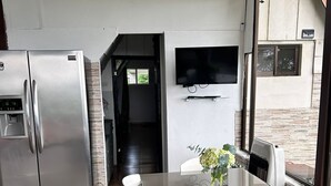A modern kitchen with a stainless steel refrigerator, a glass dining table with white chairs, and a flat-screen TV mounted on the wall. - Cozy cabin surrounded by nature with breathtaking views for total relaxation (Heredia Province)
