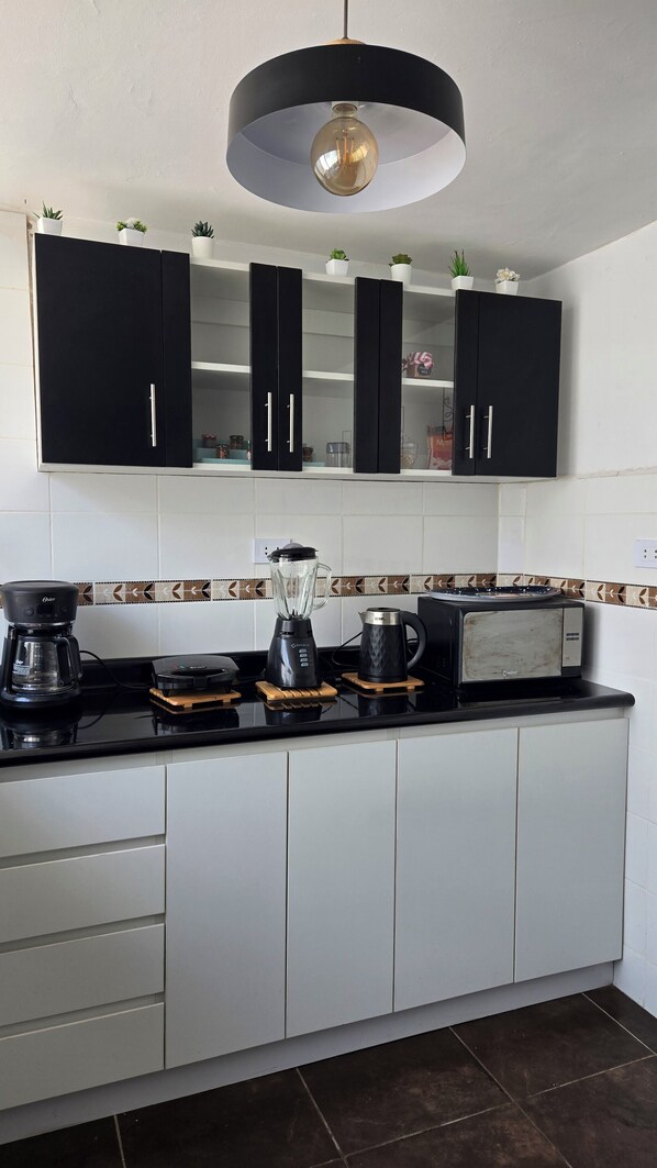 Une cuisine moderne avec des meubles de couleur noire, un plan de travail noir et un luminaire suspendu.