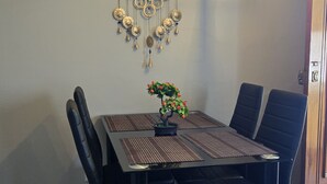 Un área de comedor con una mesa rectangular, sillas negras, una planta en maceta, un adorno en la pared y una lámpara moderna.